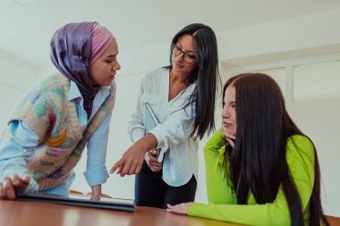 Bir grup iş kadını tesettür takıyor, birlikte kağıtları ve dizüstü bilgisayarı inceliyor, yeni iş projeleri yaratıyor, takım çalışması, işbirliği ve verimliliği gösteriyor.