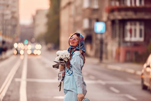 迷人的女人穿着精致的蓝色传统服装 提着蓝色的手提包和一束鲜花 在夕阳西下优雅地在城市里漫步 营造出迷人的景色 — 图库照片
