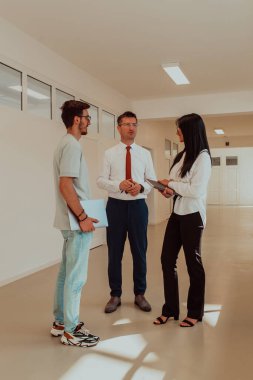 Direktör, büyük bir şirketin modern ve geniş bir koridorunda sekreter ve genç bir programcıyla çeşitli iş konuları ve projeler hakkında bir konuşma yapar.