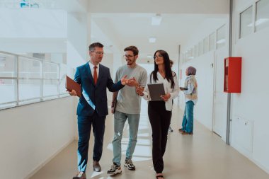 Direktör, büyük bir şirketin modern ve geniş bir koridorunda sekreter ve genç bir programcıyla çeşitli iş konuları ve projeler hakkında bir konuşma yapar.