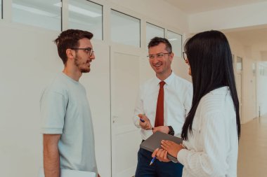 Direktör, büyük bir şirketin modern ve geniş bir koridorunda sekreter ve genç bir programcıyla çeşitli iş konuları ve projeler hakkında bir konuşma yapar.