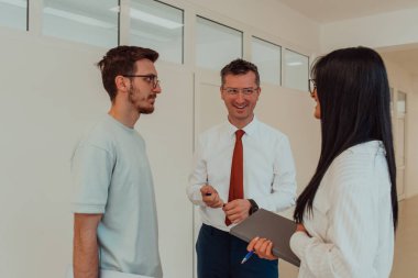 Direktör, büyük bir şirketin modern ve geniş bir koridorunda sekreter ve genç bir programcıyla çeşitli iş konuları ve projeler hakkında bir konuşma yapar.