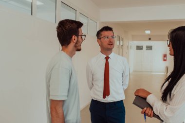 Direktör, büyük bir şirketin modern ve geniş bir koridorunda sekreter ve genç bir programcıyla çeşitli iş konuları ve projeler hakkında bir konuşma yapar.