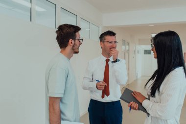 Direktör, büyük bir şirketin modern ve geniş bir koridorunda sekreter ve genç bir programcıyla çeşitli iş konuları ve projeler hakkında bir konuşma yapar.