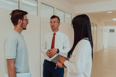 Direktör, büyük bir şirketin modern ve geniş bir koridorunda sekreter ve genç bir programcıyla çeşitli iş konuları ve projeler hakkında bir konuşma yapar.