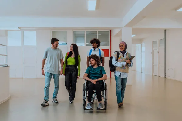 stock image In a modern university, a diverse group of students, including an Afro-American student and a hijab-wearing woman, walk together in the hallway, accompanied by their wheelchair-bound colleague