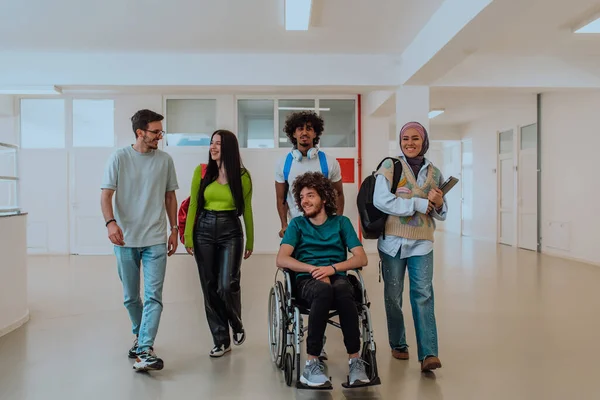 stock image In a modern university, a diverse group of students, including an Afro-American student and a hijab-wearing woman, walk together in the hallway, accompanied by their wheelchair-bound colleague