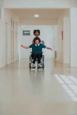 Afro-Amerikan hastane teknisyeni hastane koridorlarında şefkatle geziniyor, tekerlekli sandalyeye mahkum iş arkadaşını itiyor, birlik, destek ve kapsayıcılığı simgeliyor.. 