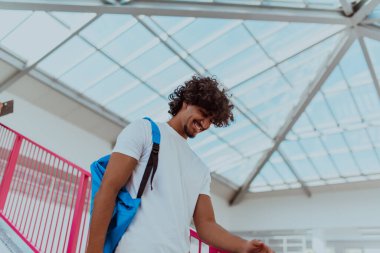 Mavi sırt çantalı Afrikalı bir öğrenci, modern Afro saç stili ve geniş bir gülümsemeye sahip, coşku yayıyor ve modern bir üniversitenin coşkulu ruhunu temsil ediyor, hırsını somutlaştırıyor.