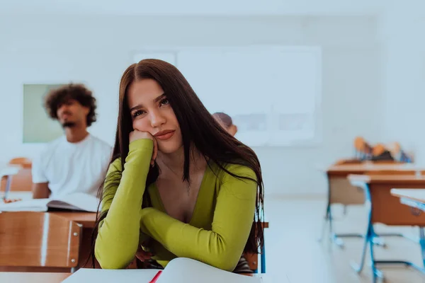A weary-looking student sitting in front of a group of diverse students in a modern classroom, capturing the blend of exhaustion, learning, and collaboration in their academic journey.