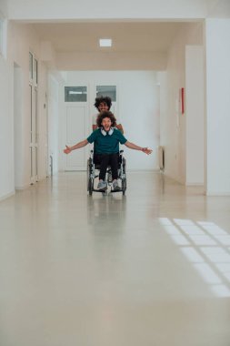 Afro-Amerikan hastane teknisyeni hastane koridorlarında şefkatle geziniyor, tekerlekli sandalyeye mahkum iş arkadaşını itiyor, birlik, destek ve kapsayıcılığı simgeliyor.. 