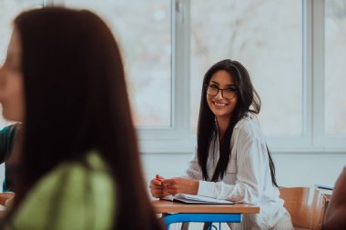 Gözlük takan siyah saçlı bir kız öğrenci, modern bir sınıfta dikkatle eğitime ve öğrenmeye odaklanmış ve merakla yaklaşmaktadır.. 