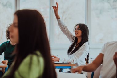 Gözlük takan siyah saçlı bir kız öğrenci, modern bir sınıfta dikkatle eğitime ve öğrenmeye odaklanmış ve merakla yaklaşmaktadır.. 