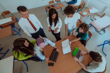Çeşitli öğrencilerden oluşan bir grubun en iyi görüntüsü modern bir okul sınıfında toplanıyor, çeşitli projeler hakkında ateşli tartışmalar yapıyorlar, takım çalışmasını kucaklıyorlar ve teknolojiden yararlanıyorlar.