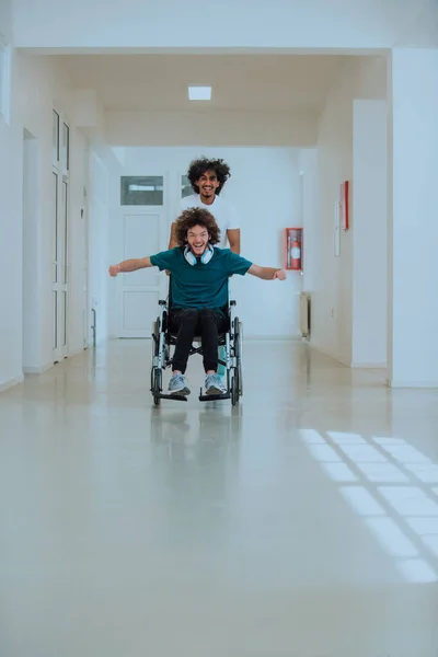 Afro-Amerikan hastane teknisyeni hastane koridorlarında şefkatle geziniyor, tekerlekli sandalyeye mahkum iş arkadaşını itiyor, birlik, destek ve kapsayıcılığı simgeliyor.. 