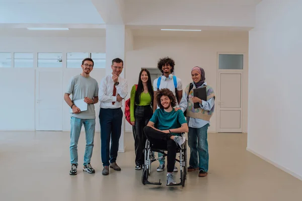 stock image A group of students with a professor and a colleague who is in a wheelchair are standing together in the corridor of a modern university.