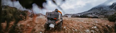 Bir adamın geniş fotoğrafı korkusuzca bir ATV Avlusu 'nda tehlikeli karlı arazide maceralı bir yolculuğun tadını çıkarıyor, zorlu dağ manzarasının heyecanını ve heyecanını kucaklıyor.. 