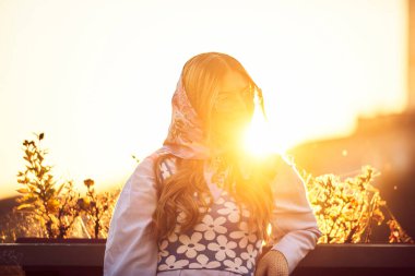 Zarif, mavi, geleneksel bir elbiseyle süslenmiş bir kadının cazibesi. Elinde mavi bir çanta ve bir buket çiçekle gün batımında zarif bir şekilde şehirde gezinerek büyüleyici bir manzara yaratıyor.