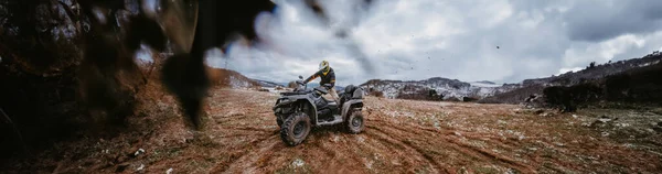 男性の広い写真は 危険な雪の地形を介してAtvクワッドで冒険的な乗り心地を楽しんでおり 挑戦的な山の風景のスリルと興奮を取り入れています — ストック写真