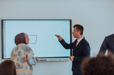 Orta karar giyinmiş bir profesör, dikkatle dinleyen öğrencileri eğitip sınıfta bilgi paylaşımı ve odaklanmış öğrenme dinamik bir sahne yaratıyor.