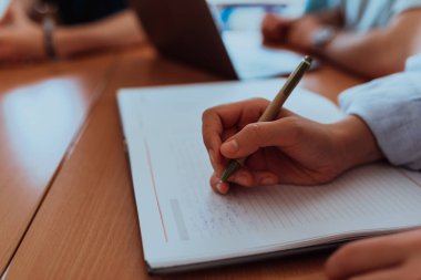 Bir kadın el, iş arkadaşlarıyla şirket sorunlarını çözme, etkili takım çalışmalarını tasvir etme, iletişim kurma gibi konuları tartışırken önemli iş fikirlerini özenle not defterine kaydeder.