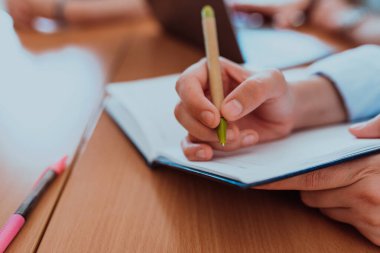 Bir kadın el, iş arkadaşlarıyla şirket sorunlarını çözme, etkili takım çalışmalarını tasvir etme, iletişim kurma gibi konuları tartışırken önemli iş fikirlerini özenle not defterine kaydeder.