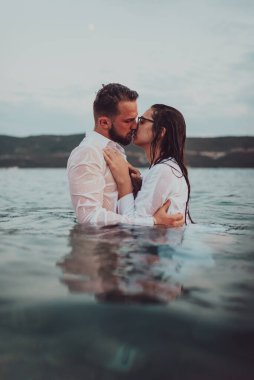 Günbatımında okyanusun dingin güzelliği arasında tutkulu bir öpücüğü paylaşan romantik genç bir çift.