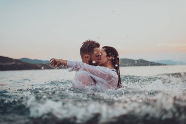 Günbatımında okyanusun dingin güzelliği arasında tutkulu bir öpücüğü paylaşan romantik genç bir çift.