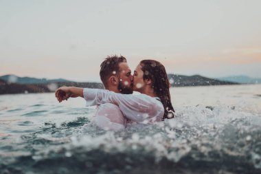 Günbatımında okyanusun dingin güzelliği arasında tutkulu bir öpücüğü paylaşan romantik genç bir çift.