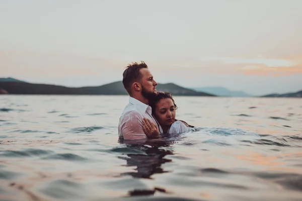 Günbatımında okyanusun dingin güzelliği arasında tutkulu bir öpücüğü paylaşan romantik genç bir çift.