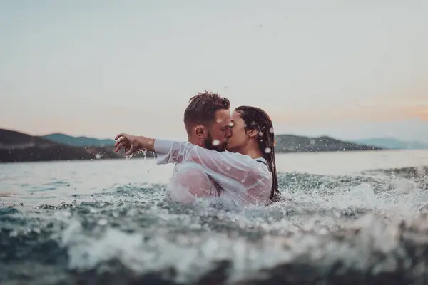 Günbatımında okyanusun dingin güzelliği arasında tutkulu bir öpücüğü paylaşan romantik genç bir çift.