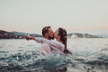 Günbatımında okyanusun dingin güzelliği arasında tutkulu bir öpücüğü paylaşan romantik genç bir çift.