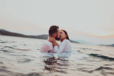 Günbatımında okyanusun dingin güzelliği arasında tutkulu bir öpücüğü paylaşan romantik genç bir çift.