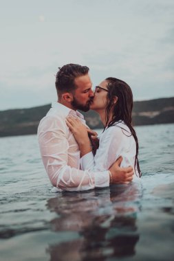 Günbatımında okyanusun dingin güzelliği arasında tutkulu bir öpücüğü paylaşan romantik genç bir çift.