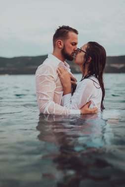 Günbatımında okyanusun dingin güzelliği arasında tutkulu bir öpücüğü paylaşan romantik genç bir çift.