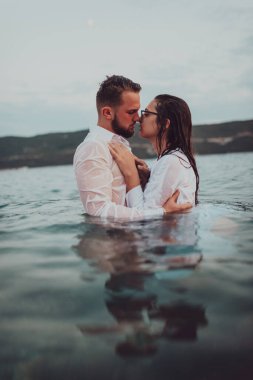 Günbatımında okyanusun dingin güzelliği arasında tutkulu bir öpücüğü paylaşan romantik genç bir çift.