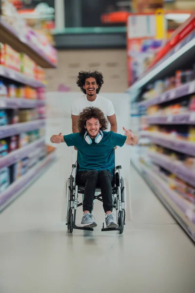 In a large supermarket, an African American man compassionately pushes his friend in a wheelchair, showcasing a heartwarming display of friendship and support during their shopping trip.