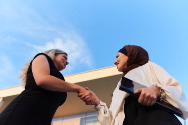 Gerçek bir hayat sahnesinde, emlak işçisi olan tesettürlü Müslüman bir kadın, başarılı bir şekilde mülkünü sattıktan sonra sarışın bir kadınla el sıkışıyor.. 