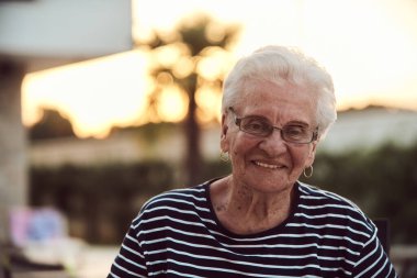 Filtresiz bir portre, gerçek bir yaşlı kadın zarif bir şekilde bir sandalyede oturur, kırışıklıklar ve doğal bir yüzle yaşlanmanın gerçekliğini gösterir.. 