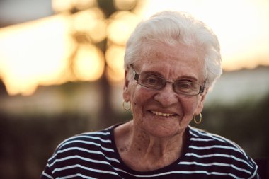 Filtresiz bir portre, gerçek bir yaşlı kadın zarif bir şekilde bir sandalyede oturur, kırışıklıklar ve doğal bir yüzle yaşlanmanın gerçekliğini gösterir.. 