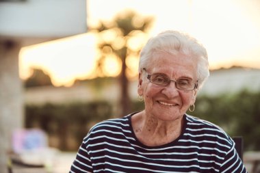 Filtresiz bir portre, gerçek bir yaşlı kadın zarif bir şekilde bir sandalyede oturur, kırışıklıklar ve doğal bir yüzle yaşlanmanın gerçekliğini gösterir.. 