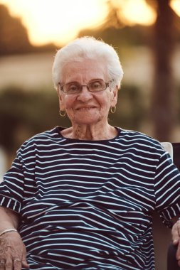 Filtresiz bir portre, gerçek bir yaşlı kadın zarif bir şekilde bir sandalyede oturur, kırışıklıklar ve doğal bir yüzle yaşlanmanın gerçekliğini gösterir.. 