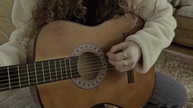 Genç, kıvırcık saçlı kız akustik gitarını evinde tutkuyla ve yetenekle çalıyor.. 