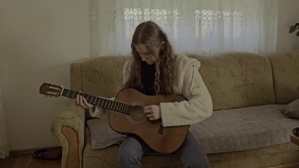 彼女の家の快適さで情熱と才能で彼女のアコースティックギターを果たしている若いカーリー髪の少女 — ストック動画
