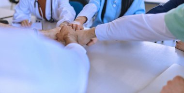 Bir grup doktor ve bir tıp hemşiresi bir masada el ele tutuşarak, sağlık alanındaki ortak çabalarını yönlendiren sarsılmaz takım çalışmasını ve dayanışmayı sergilediler.. 