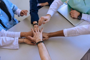 Bir grup doktor ve bir tıp hemşiresi bir masada el ele tutuşarak, sağlık alanındaki ortak çabalarını yönlendiren sarsılmaz takım çalışmasını ve dayanışmayı sergilediler.. 