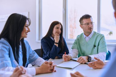 Kendini adamış bir grup doktor ve tıp hemşiresi, meslektaşlarının bir sağlık merkezindeki çalışma planlarını dikkatle dinliyor, işbirliğini teşvik ediyor ve yüksek kaliteli hasta bakımı sağlıyorlar.. 