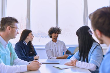 Akıllı bir tablet kullanan genç bir Afrikalı Amerikalı doktor çalışma ve hasta bakımı planını modern bir hastanedeki diğer doktorlara güvenle sunuyor.