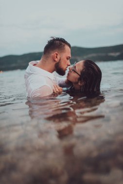 Günbatımında okyanusun dingin güzelliği arasında tutkulu bir öpücüğü paylaşan romantik genç bir çift.