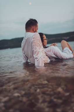 Günbatımında okyanusun dingin güzelliği arasında tutkulu bir öpücüğü paylaşan romantik genç bir çift.